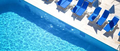 Una piscina al aire libre, sombrillas, sillones reclinables de piscina