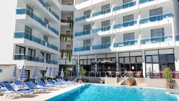 A hotel pool area with multiple levels of balconies, lounge chairs, and umbrellas.