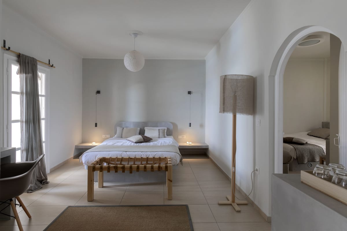 Un dormitorio moderno con una cama grande, mesitas de noche, un banco, una lámpara de pie y un espejo.