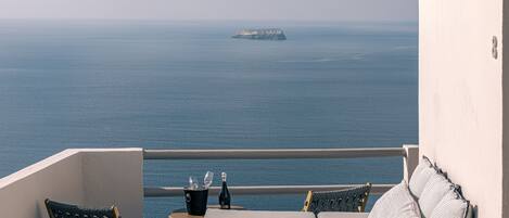 Un balcón con vista al mar, una mesa con una botella y vasos, y dos sillas.