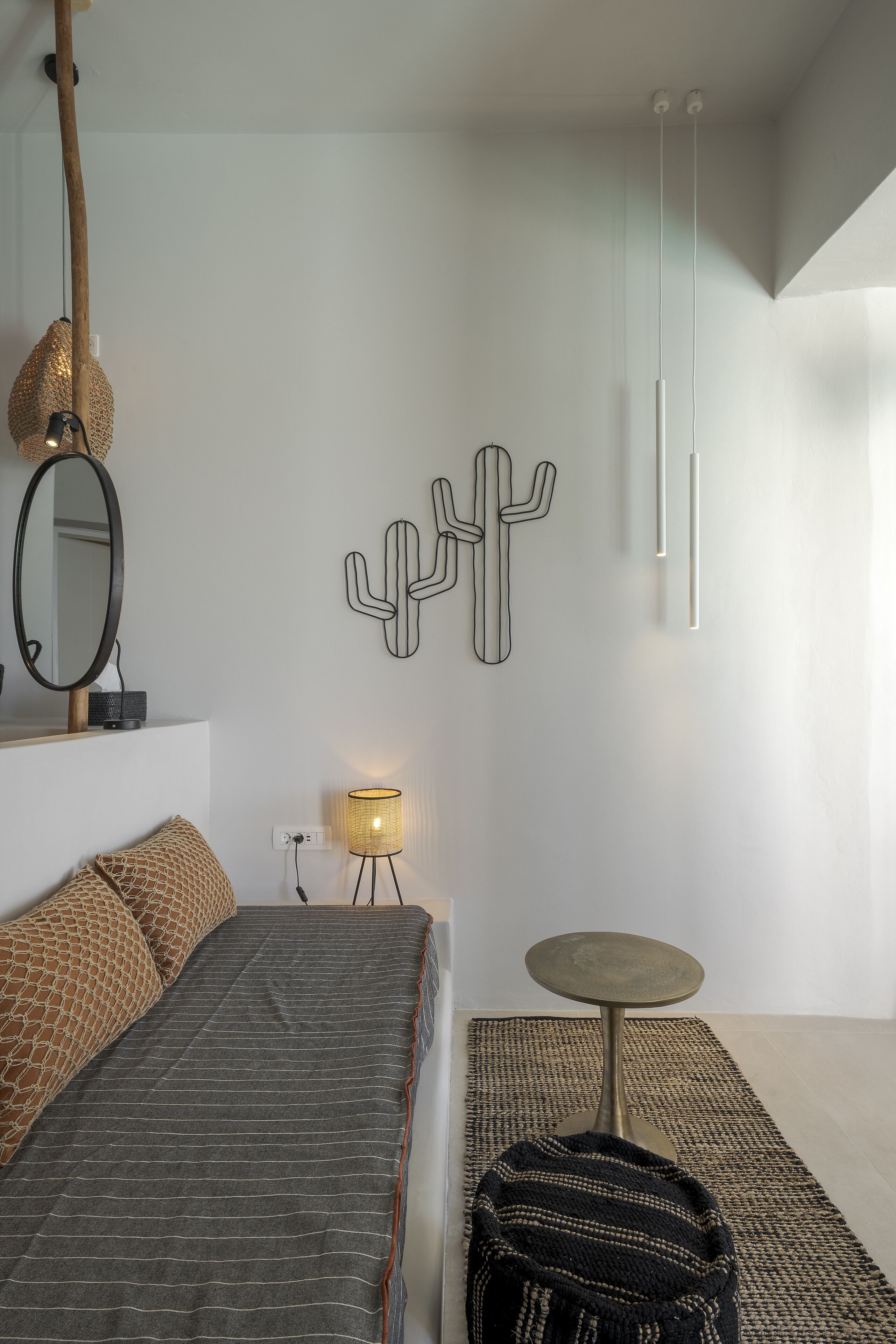 A modern bedroom with a bed, a round table, a lamp, and a cactus wall art.