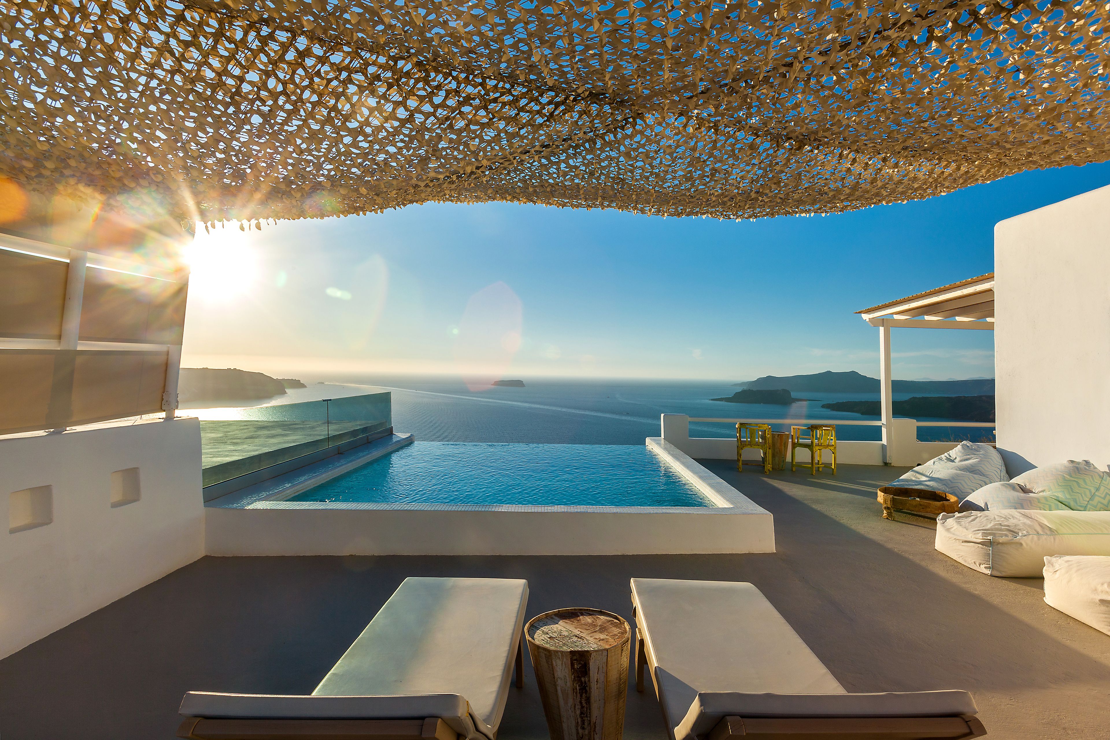 Une piscine à débordement située sur le toit, offrant une vue sur la mer, ainsi que des chaises longues et une table en bois.
