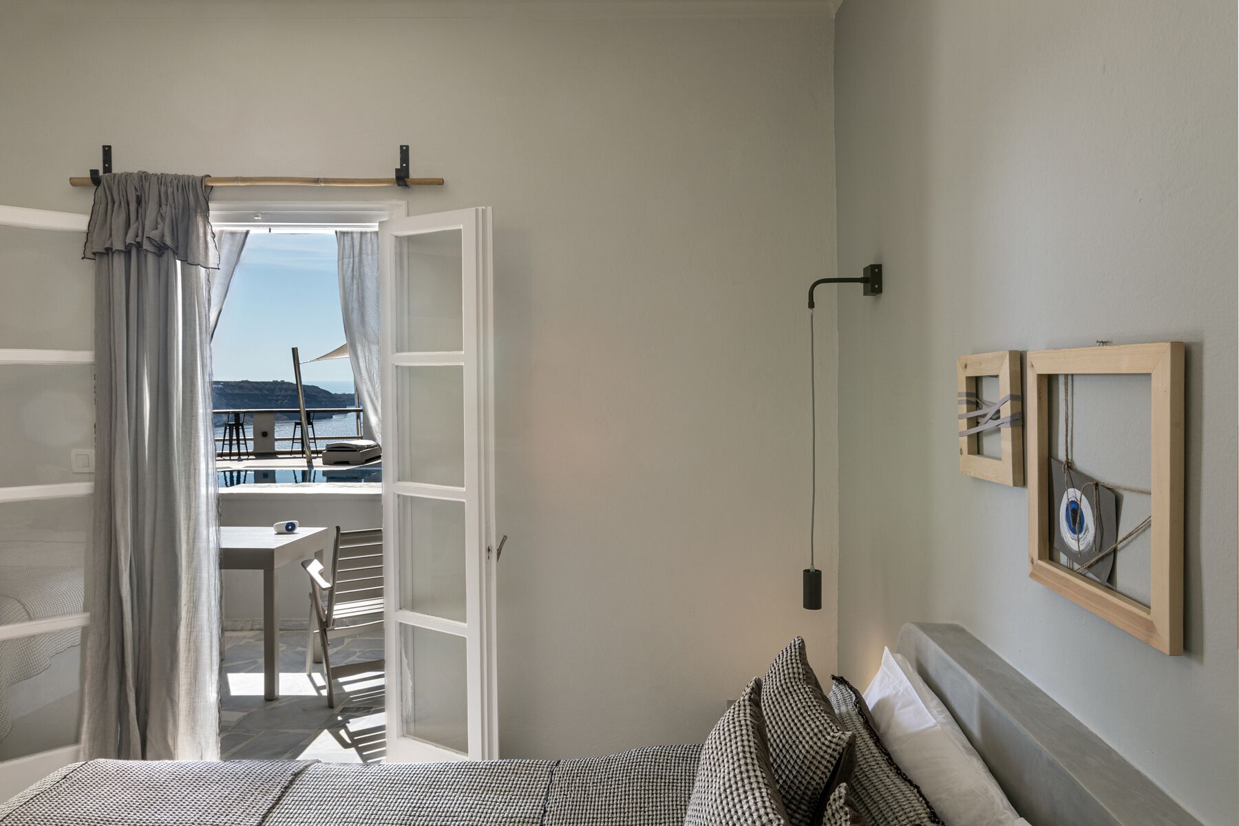 A room with a bed, a window with curtains, a view of a balcony, and a wall-mounted light fixture.