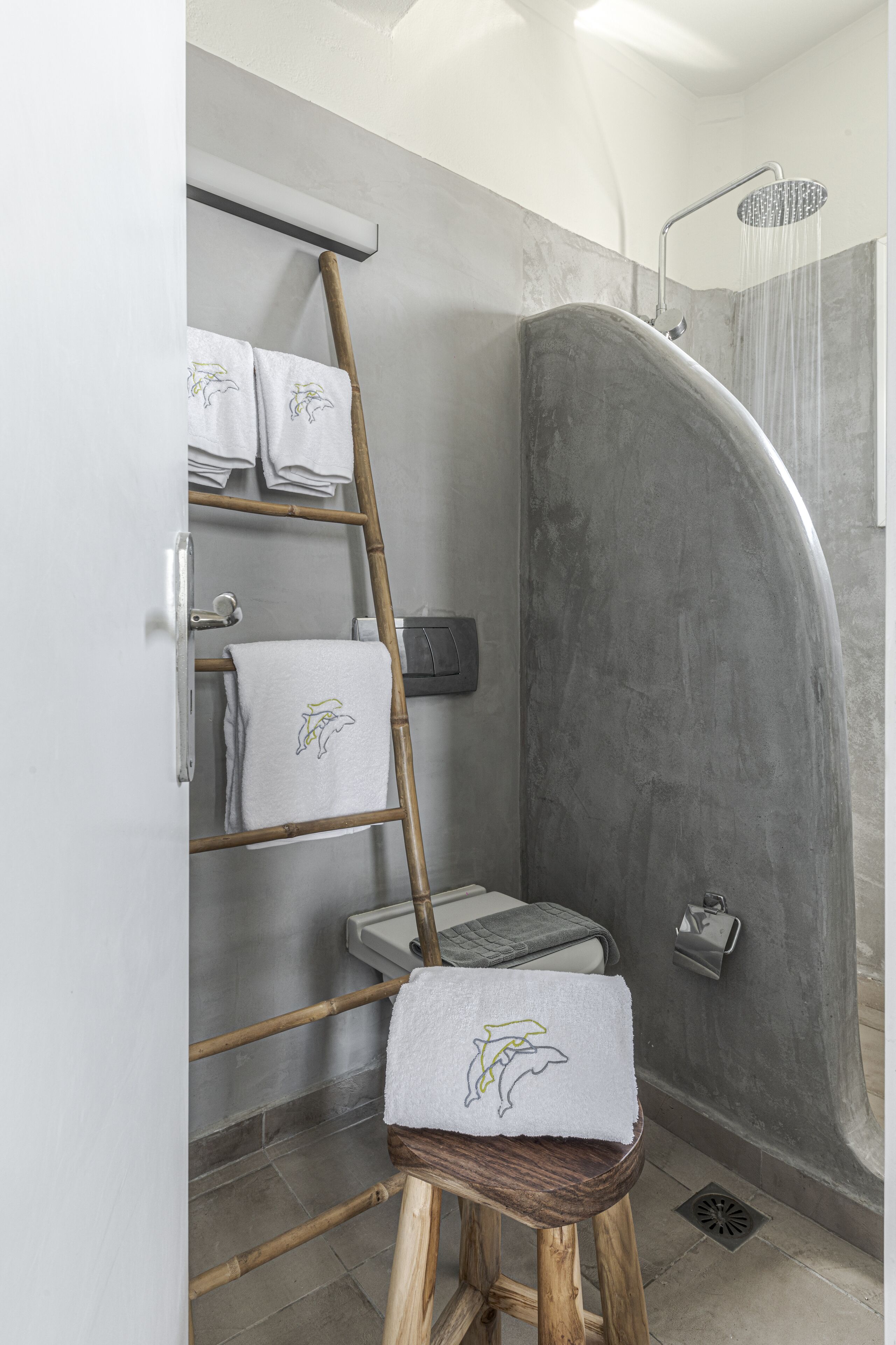 A shower area with a curved wall, a wooden ladder, and a towel rack holding multiple towels.