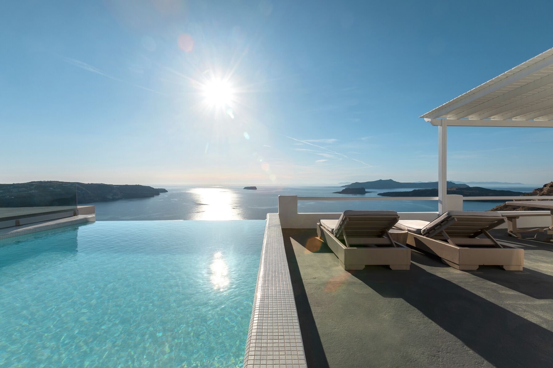 A clear blue sky, a swimming pool, and lounge chairs with a view of the sea.