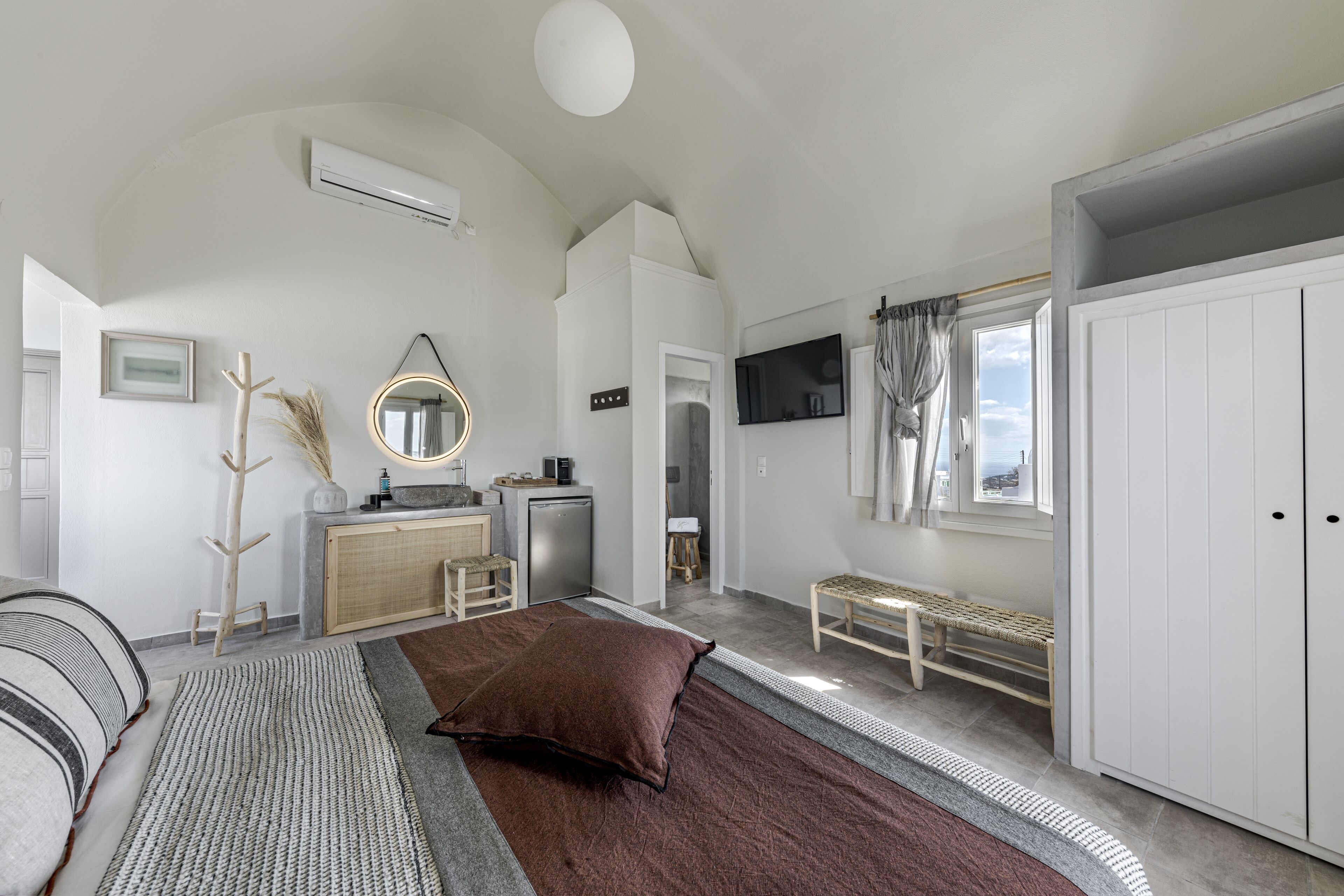 A modern bedroom with a bed, bedside table, dresser, and a large window.