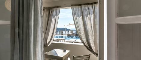 A balcony with a table and chairs, overlooking a pool and a mountainous landscape.