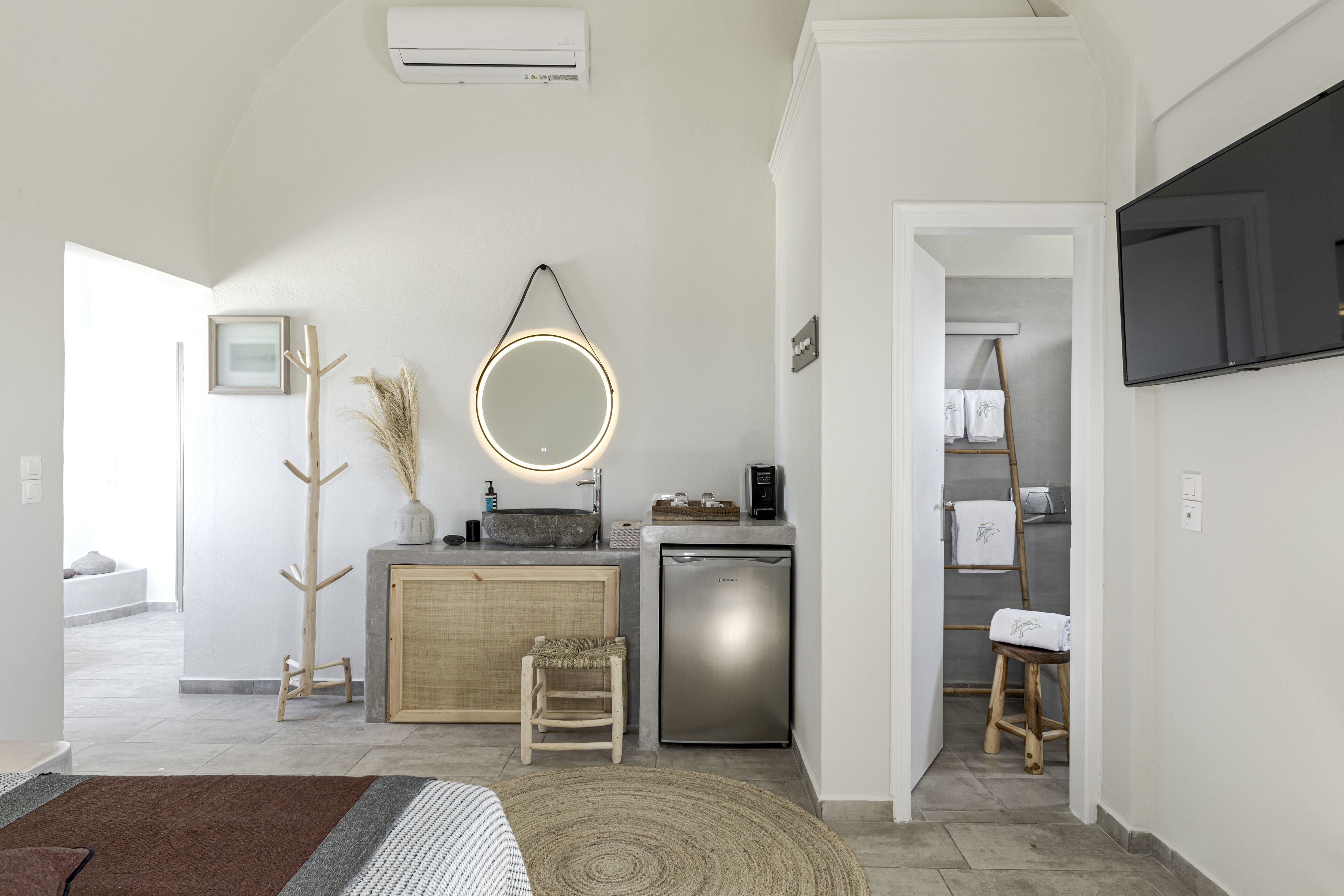 Une cuisine moderne dotée d’un réfrigérateur encastré, d’une chaise en bois et d’un miroir rond avec éclairage intégré.