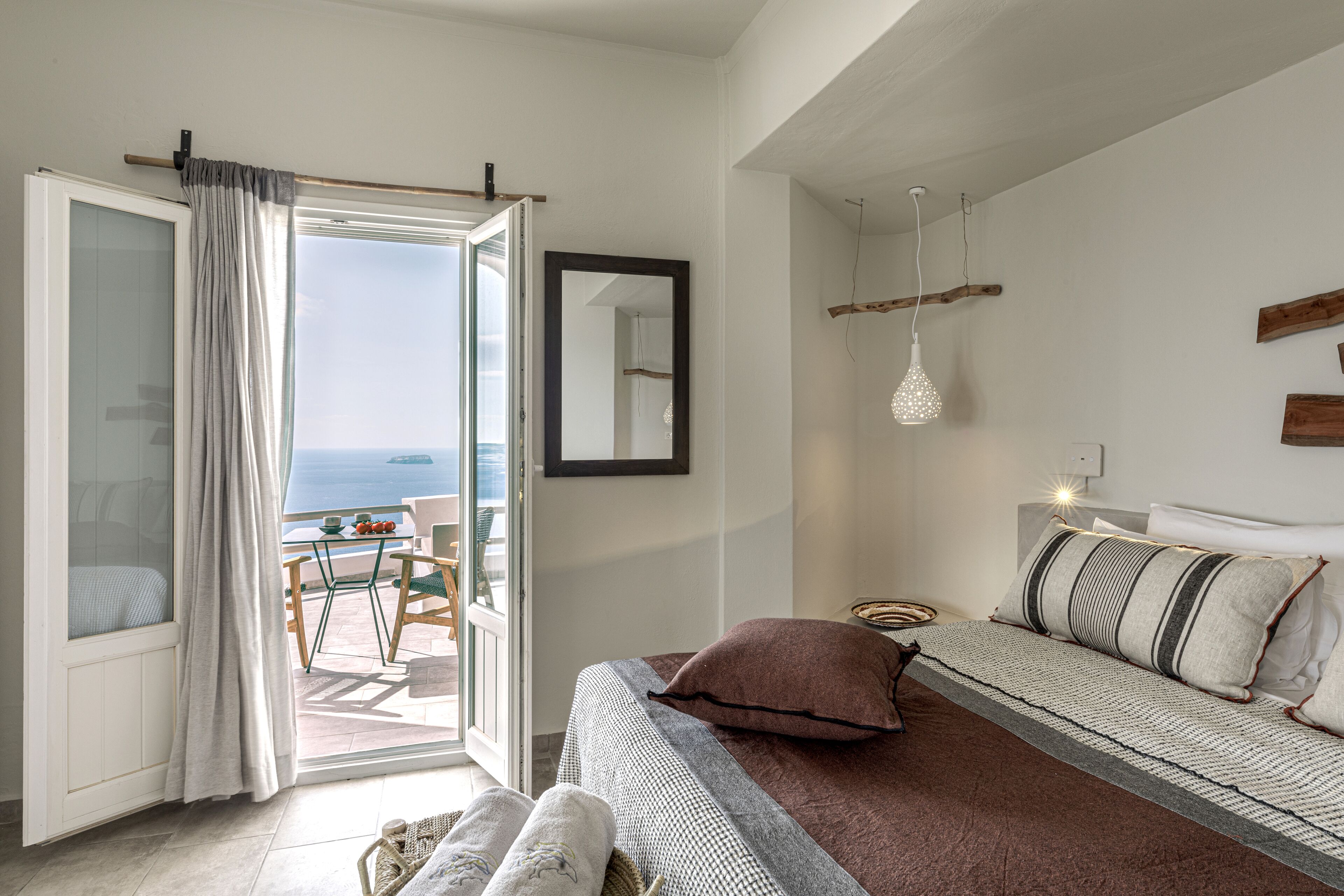 A bedroom with a bed, a view of the sea, and a balcony with a table and chairs.