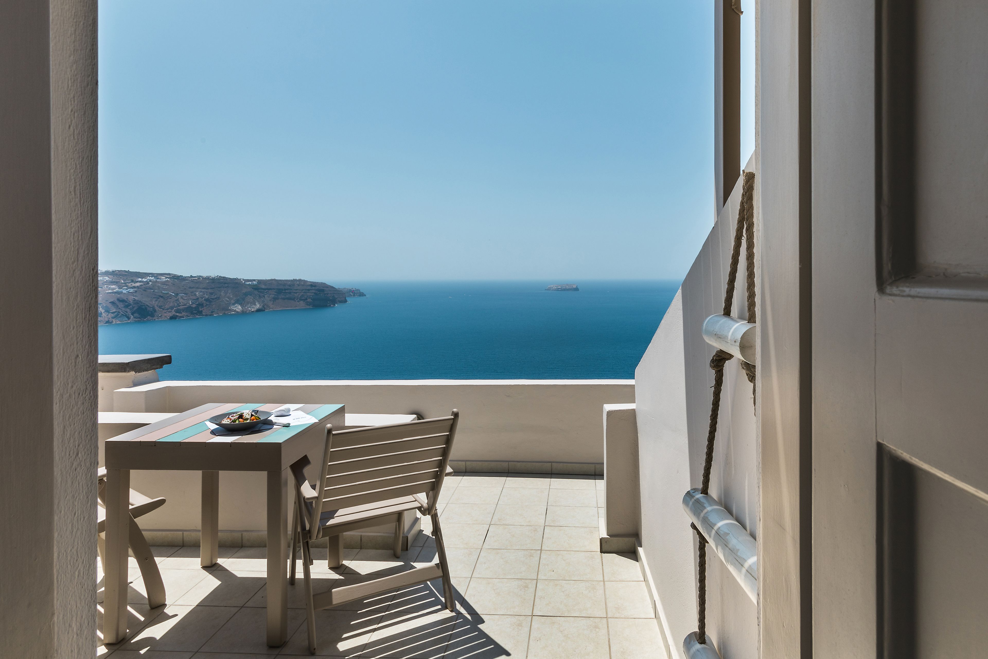 Ein Balkon mit Tisch und Stühlen, der Blick auf die Küste mit Klippen und dem Meer bietet.