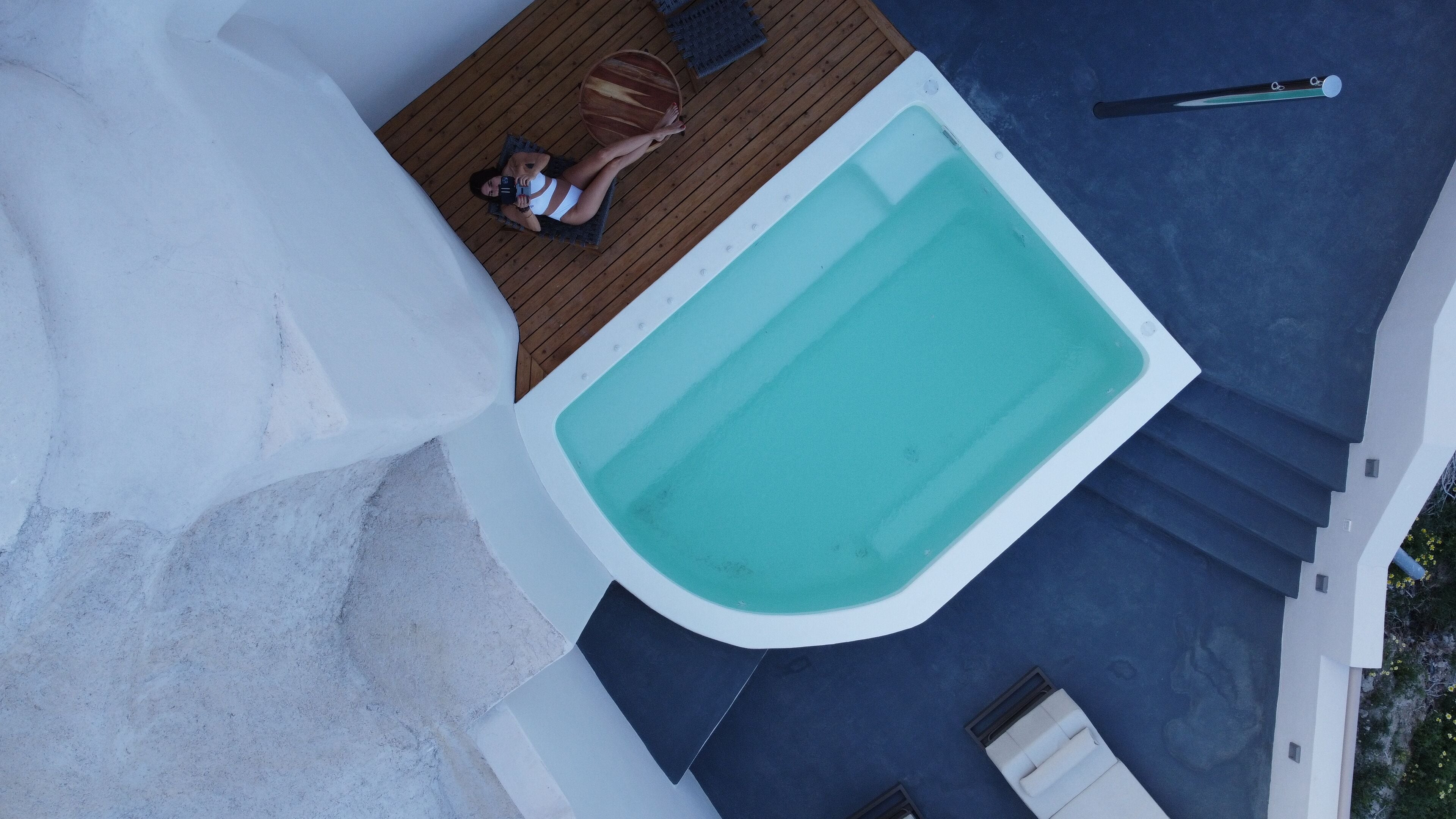 An aerial view of a swimming pool with a wooden deck, a lounge chair, and a yoga mat.