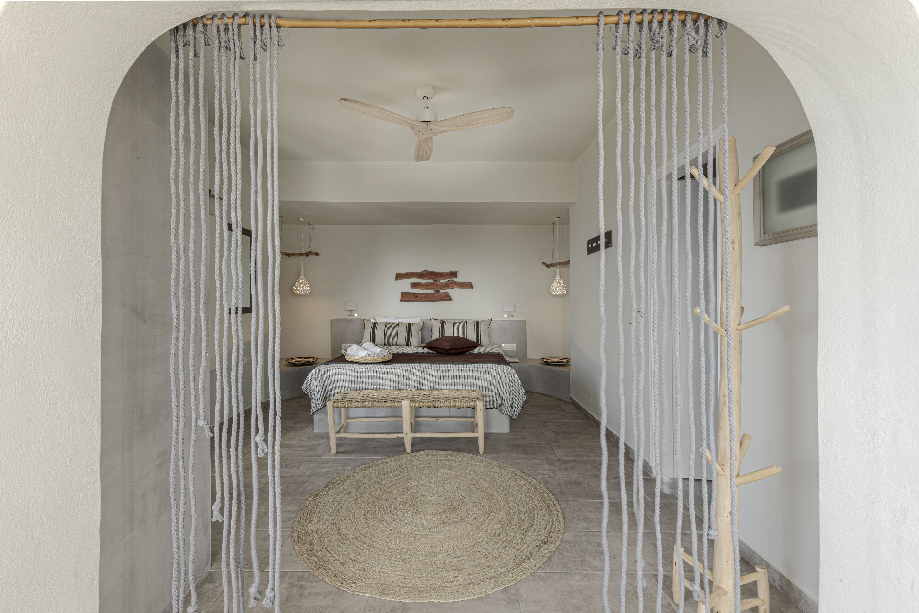 Quarto com cama, mesas de cabeceira, ventoinha no teto e tapete tecido.