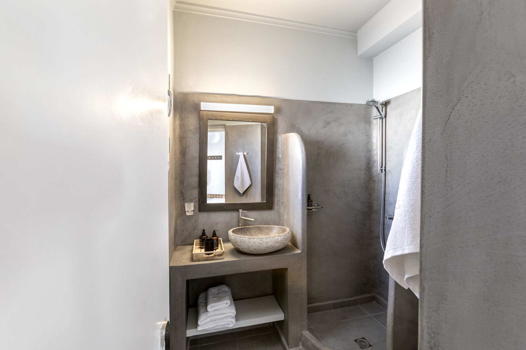 A bathroom with a stone sink, a mirror, a towel rack, and a shower.
