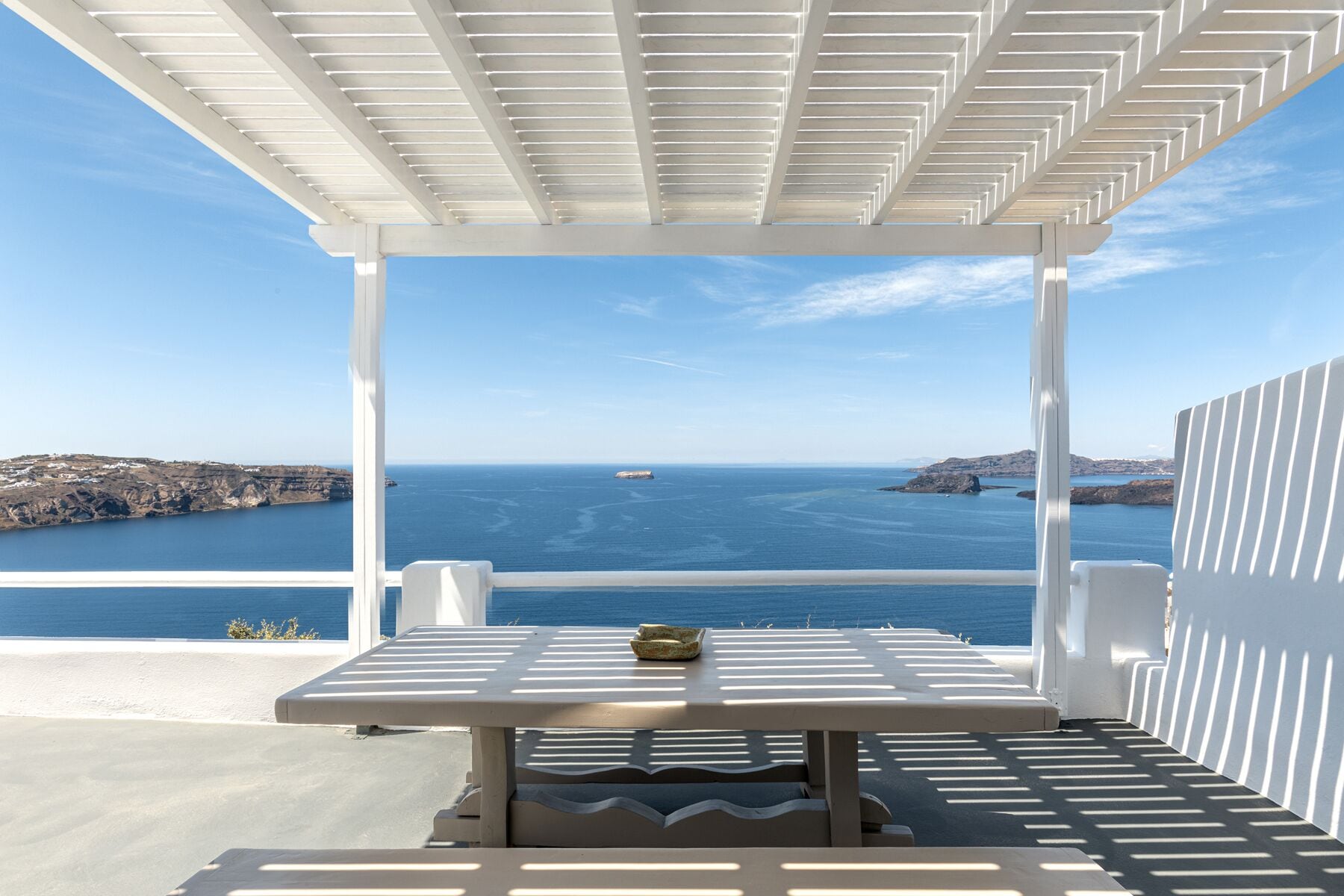Un área de estar al aire libre con una mesa y sillas, con vistas a la costa, el mar y tierra a lo lejos.
