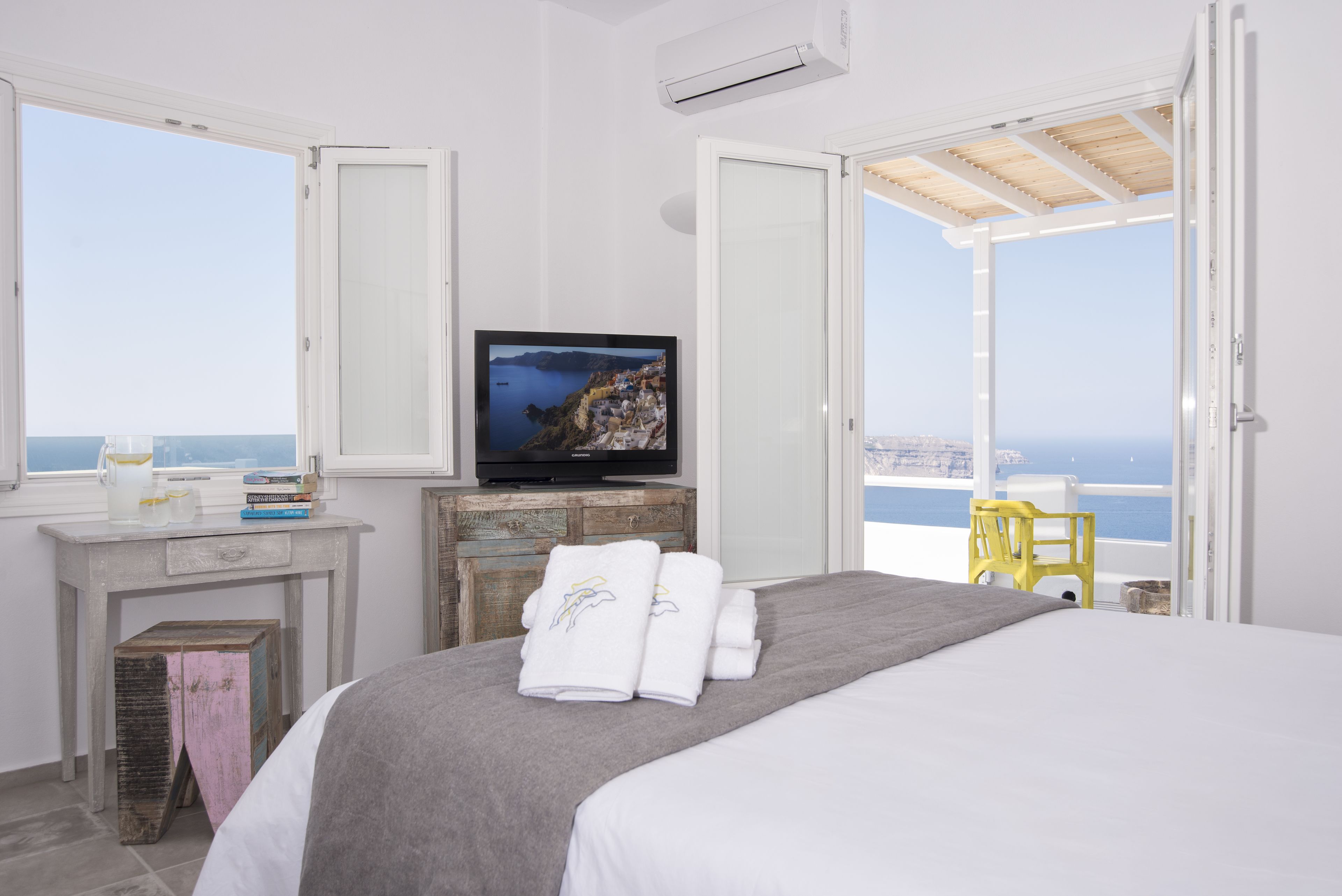A hotel room with a bed, a television, a desk with a computer, and a view of the sea.