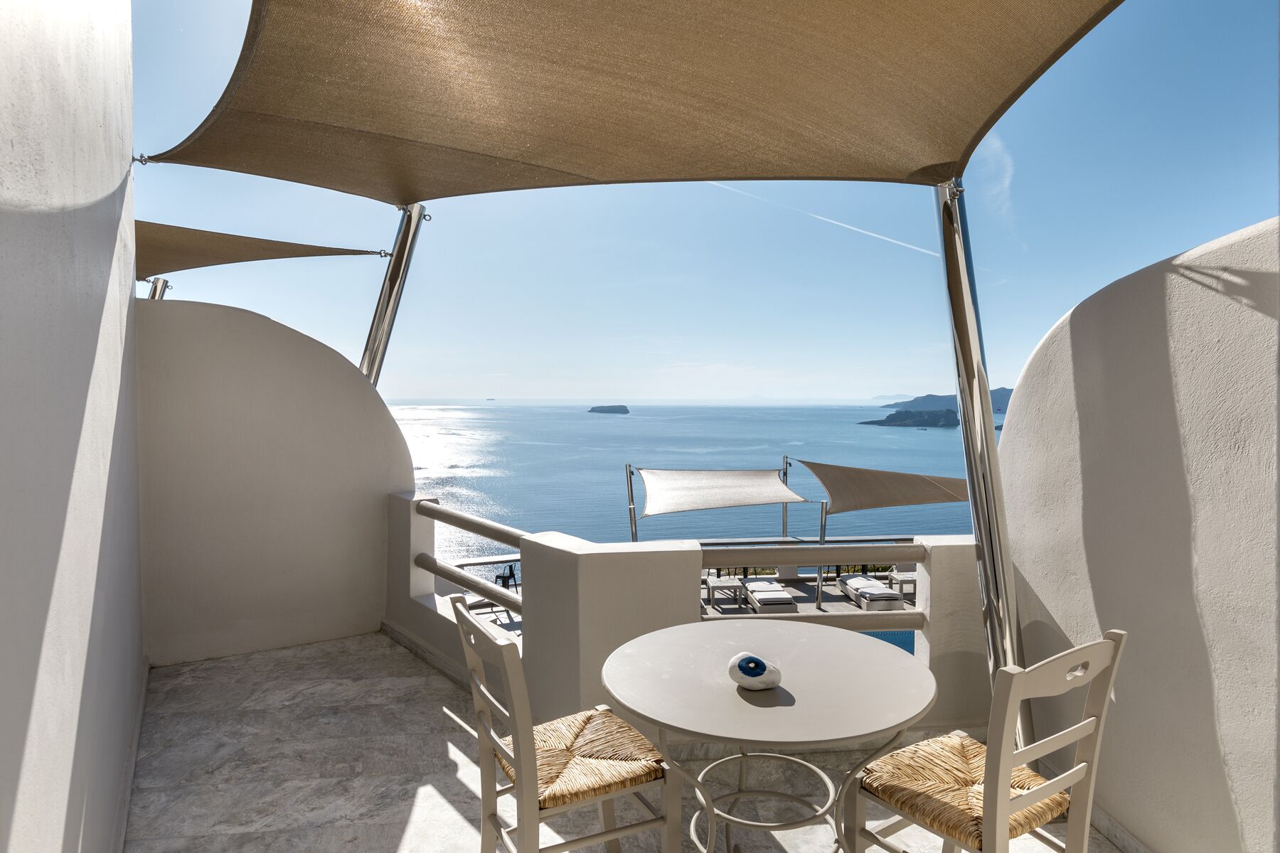 A balcony with a table and chairs, overlooking a body of water with boats and islands.