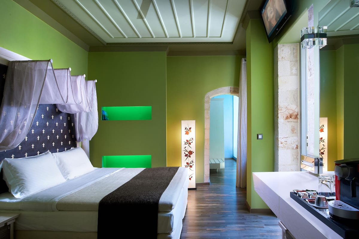 Hotelkamer met een bed, een kaptafel met spiegel, een televisie en een gang die naar een andere kamer leidt.