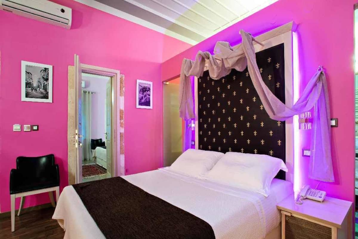 Een slaapkamer met een bed, een stoel, een nachtkastje met een lamp en een wandairconditioner.