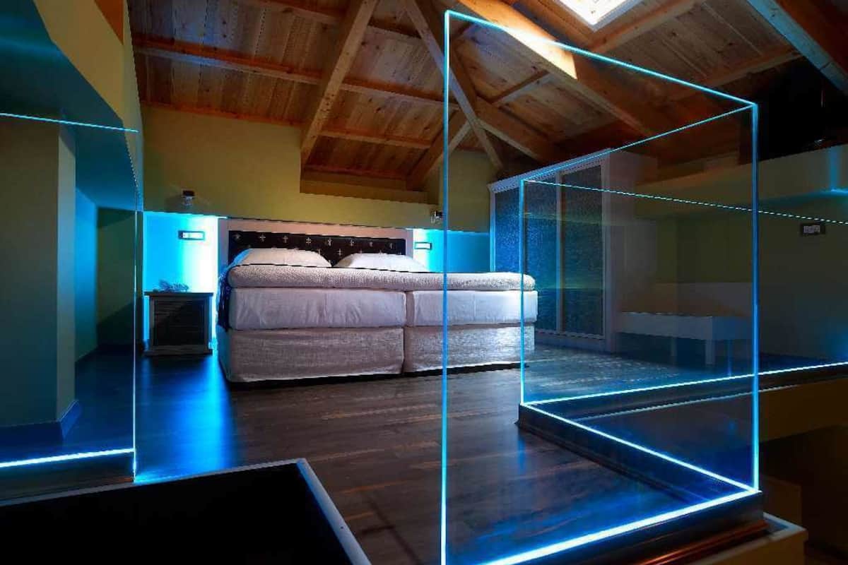Een moderne slaapkamer met een bed, houten balken in het plafond en blauwe LED-verlichting.