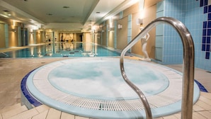 Una amplia piscina interior con un jacuzzi central, rodeada por un suelo y paredes alicatados con una decoración azul y beige.