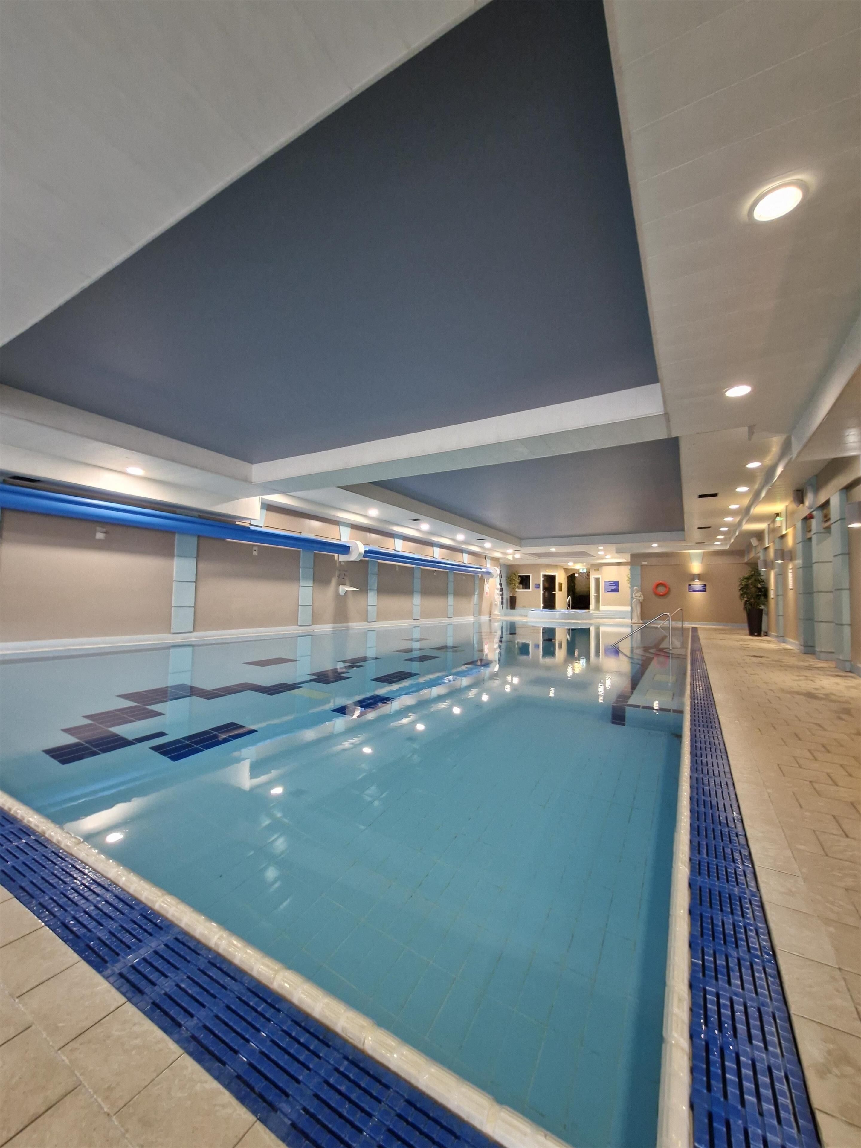Ein Hallenbad mit deutlich abgetrennten Bahnen, Fliesenboden und einer Decke mit eingelassener Beleuchtung.