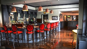 Zona de bar con una barra alargada, varios taburetes acolchados rojos e iluminación colgante de cobre.
