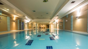 Una piscina interior larga y estrecha con suelo y paredes de azulejos, y varias puertas a lo largo de los laterales.