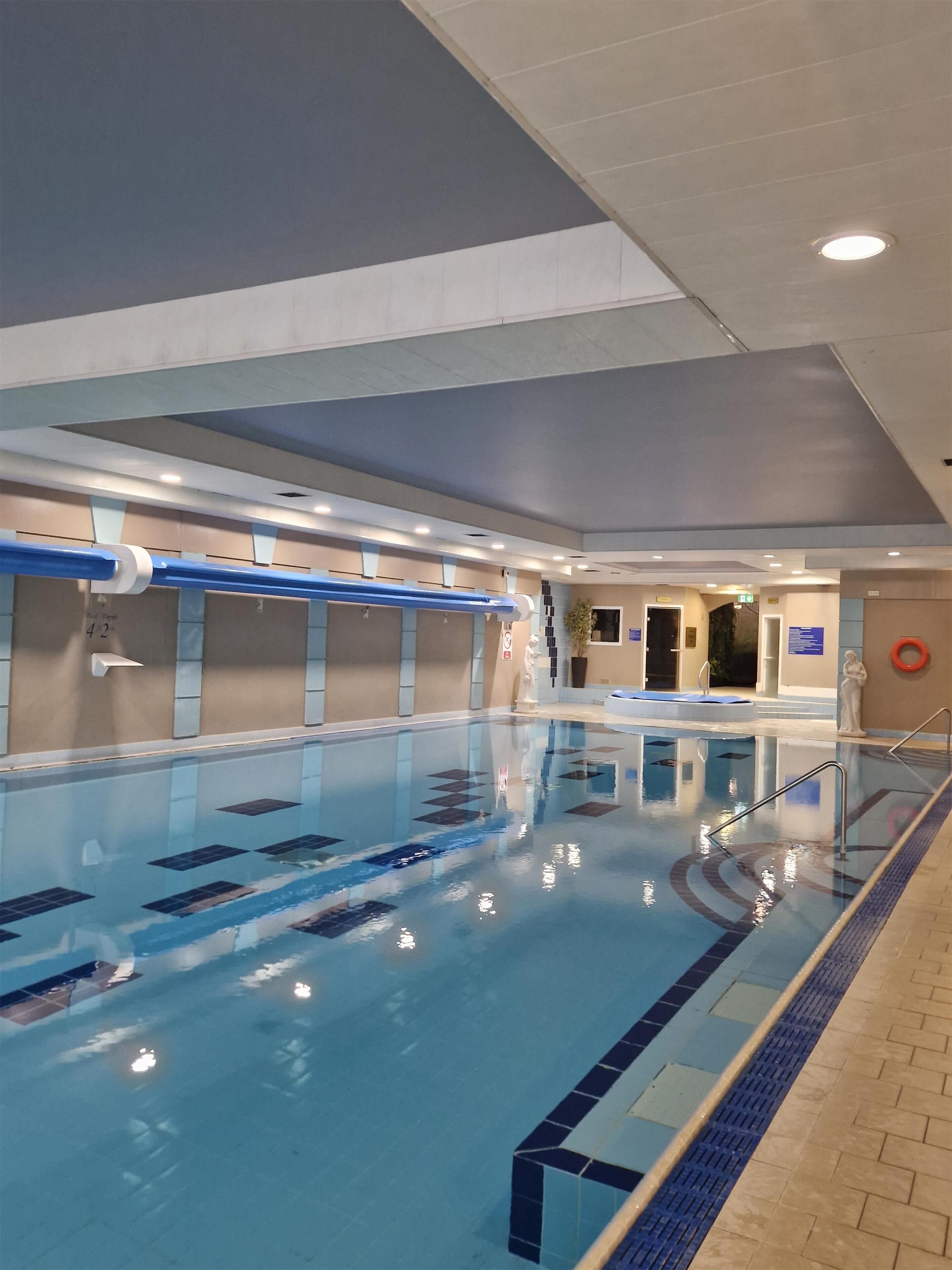 An indoor swimming pool with clear lane markings, a lifeguard chair, and a safety sign.