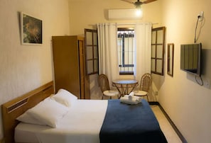 A hotel room with a bed, a small table with chairs, a television, and a window with curtains.