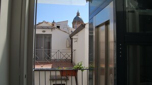 A view from a balcony with a metal railing, a small potted plant, and a glimpse of a building with a dome-shaped roof. - B&B Federico Secondo (Palermo)