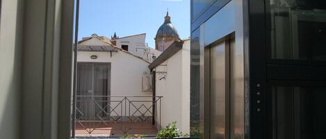 A view from a balcony with a metal railing, a small potted plant, and a glimpse of a building with a dome-shaped roof.
