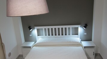 Un letto con una testiera bianca, due comodini e una lampada a sospensione.