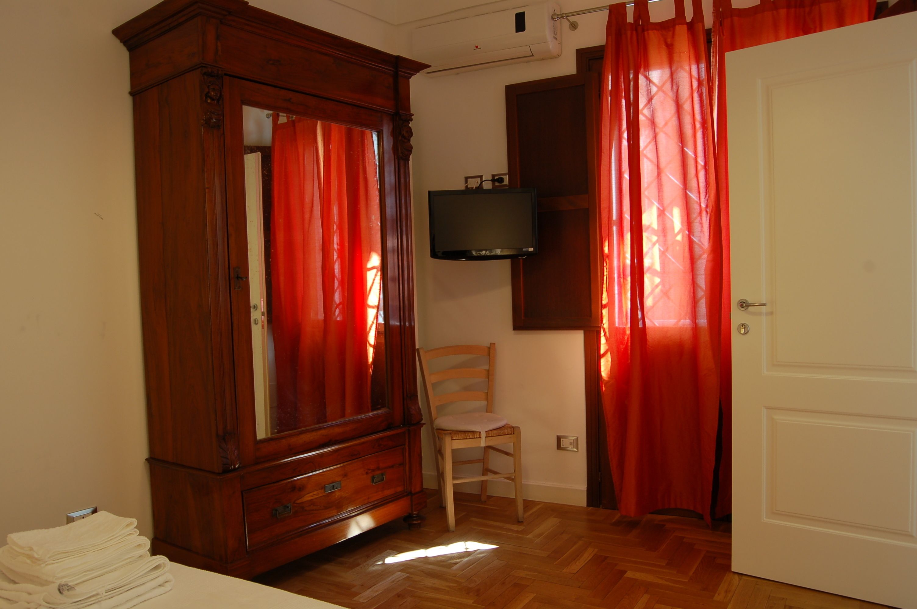 Une pièce avec une armoire en bois, un téléviseur fixé au mur, une chaise et une porte.