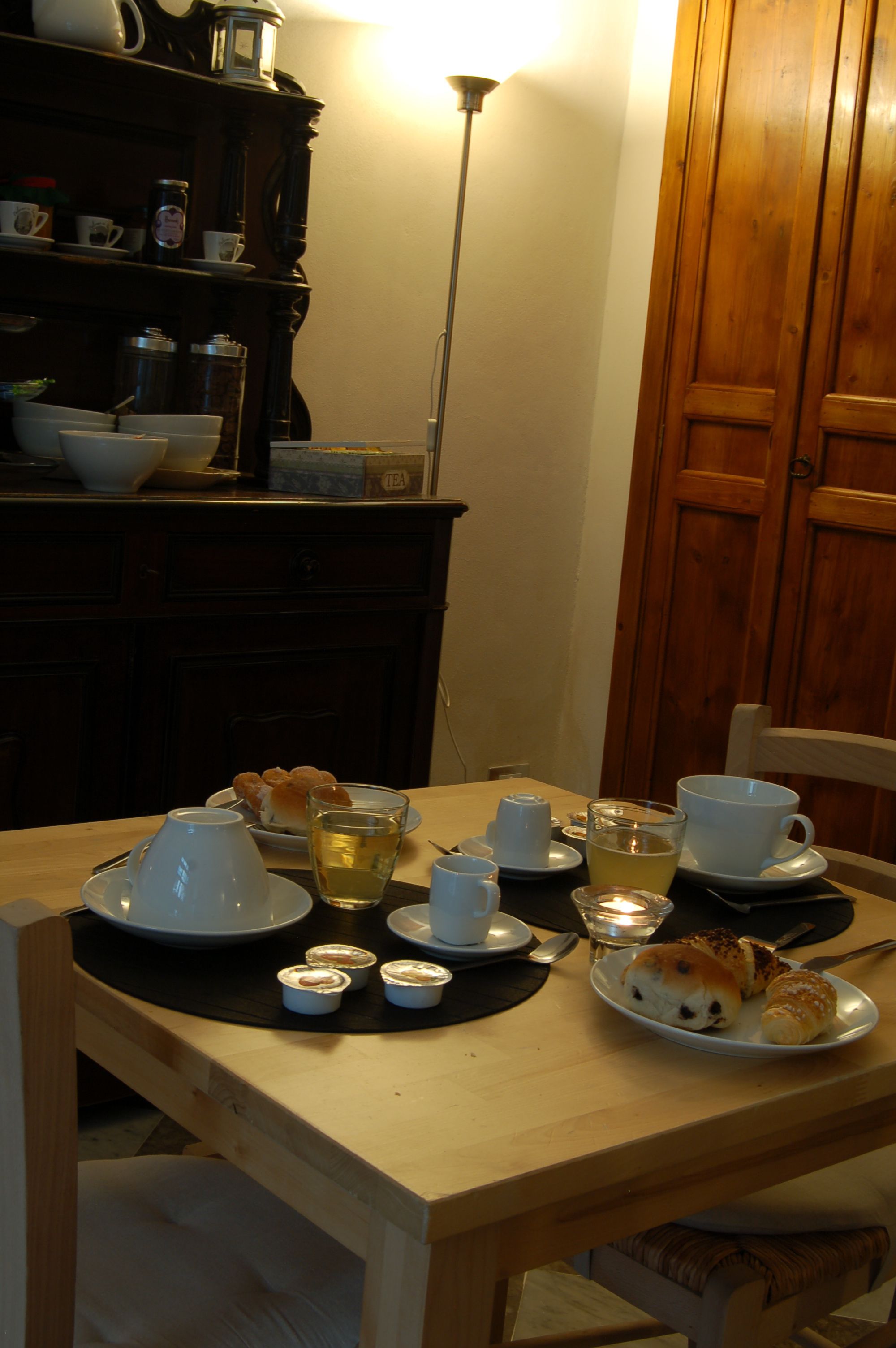 A dining table set with plates, cups, and a candle, in a room with wooden furniture and a cabinet.