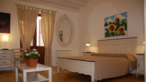 A bedroom with a bed, bedside tables, a mirror, a window with curtains, a painting of sunflowers, and a potted plant on a table. - B&B Federico Secondo (Palermo)
