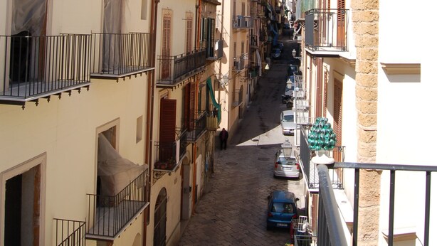 A narrow street with buildings on both sides, featuring balconies and a clear blue sky. - B&B Federico Secondo (Palermo)