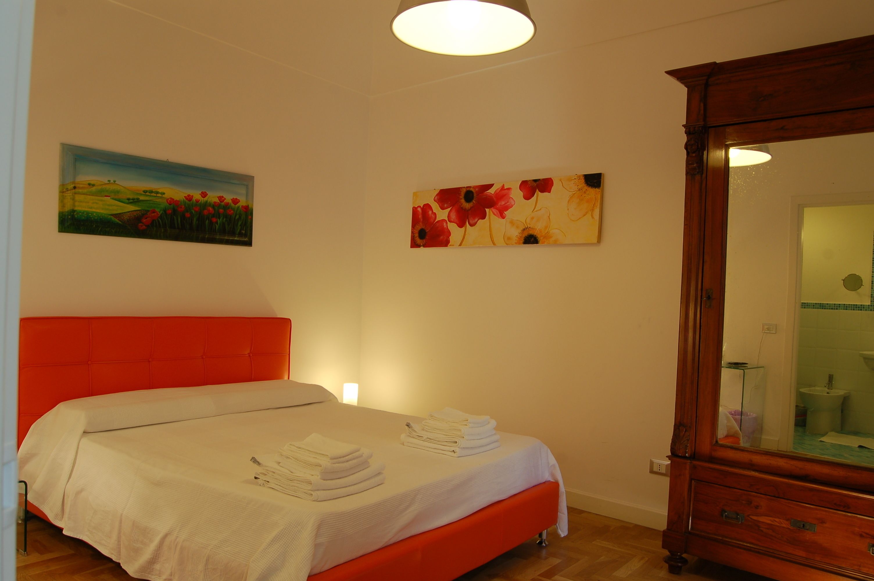Ein Schlafzimmer mit einem roten Kopfteil, einem Bett mit weißen Leinen, einer Holzkommode und zwei Bildern an der Wand.