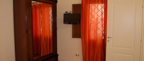A room with a wooden wardrobe, a television mounted on the wall, and a white door.
