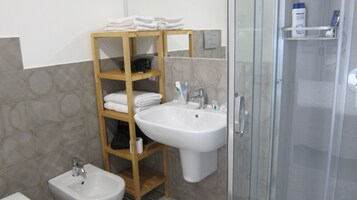 A bathroom with a wooden shelf holding towels, a sink, and a bidet.