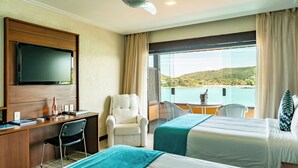 A hotel room with two beds, a desk, a chair, a TV, and a balcony with a view of the sea. - Hotel Ferradura Private (Búzios)
