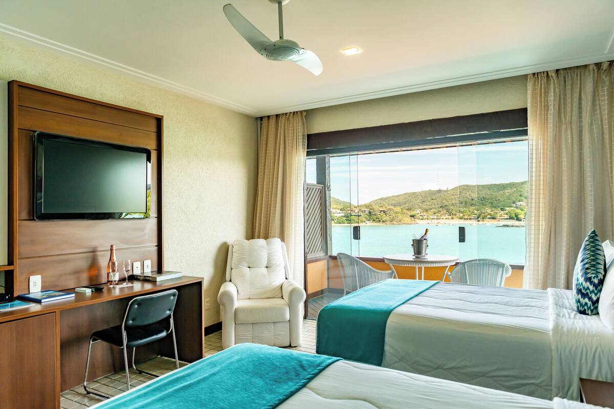 Habitación de hotel con dos camas, un escritorio, una silla, un televisor y un balcón con vista al mar.