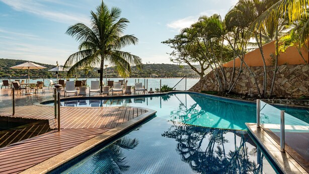 A pool area with lounge chairs and a view of the sea. - Hotel Ferradura Private (Búzios)