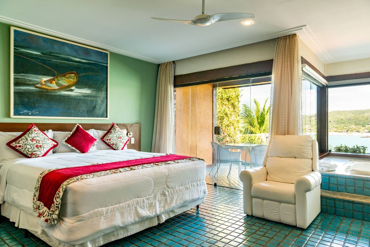 Habitación de hotel con una cama grande, una butaca reclinable, un cuadro de un barco y vistas a una piscina y follaje.