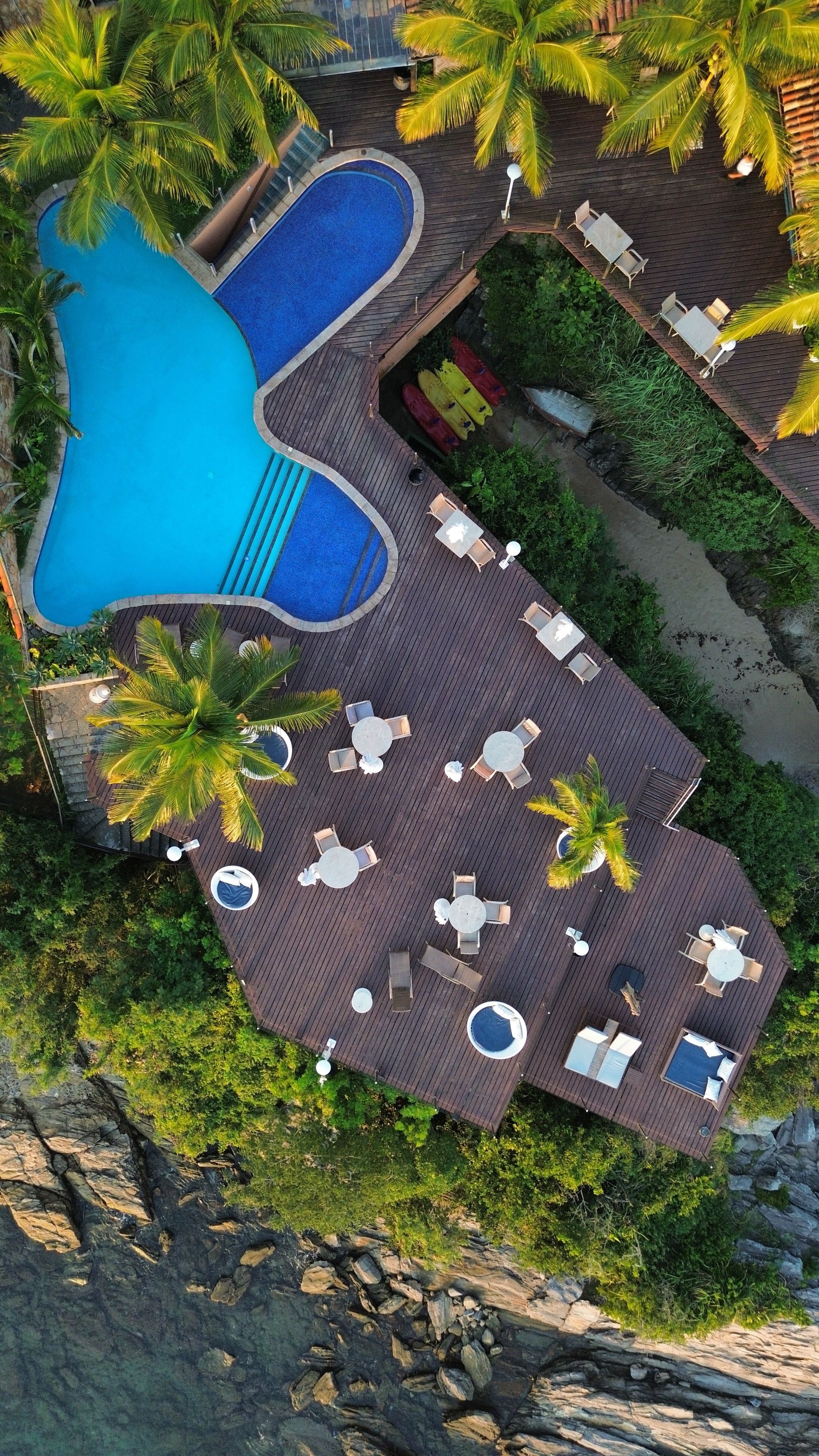 Vista aérea de un resort con una amplia piscina, varias zonas de estar con mobiliario exterior y abundante vegetación.