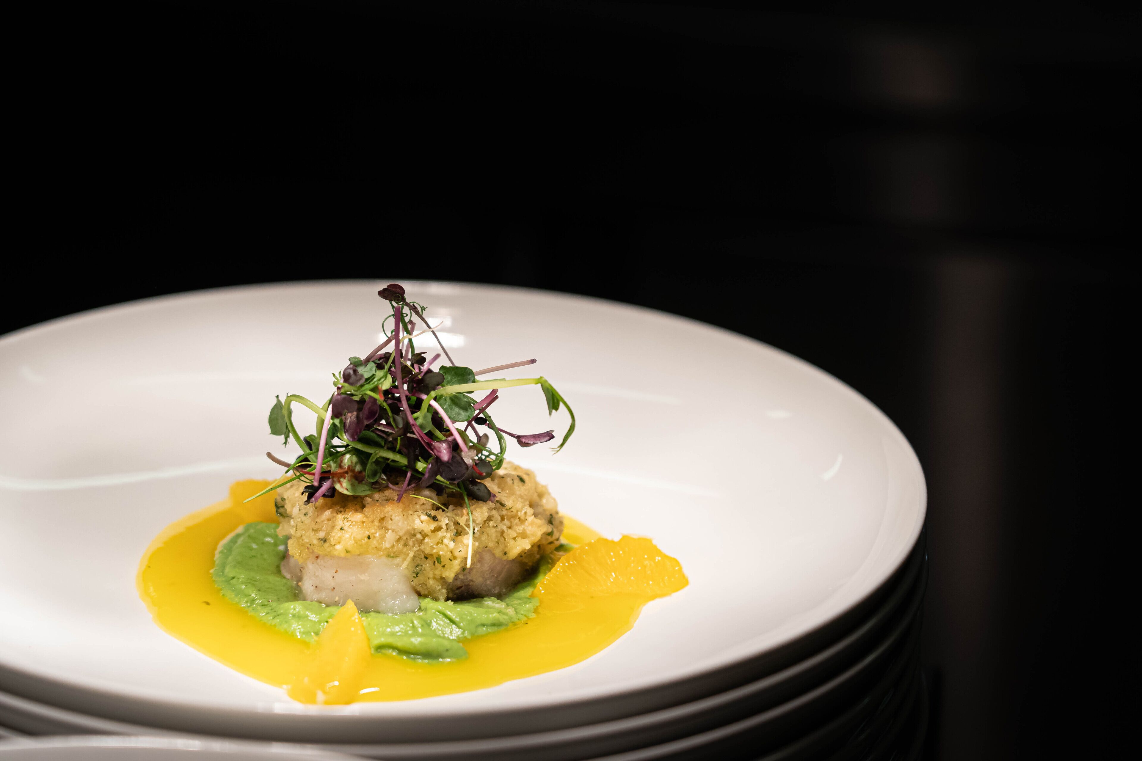Une assiette blanche contenant un plat agrémenté de verdure et d’une sauce jaune.