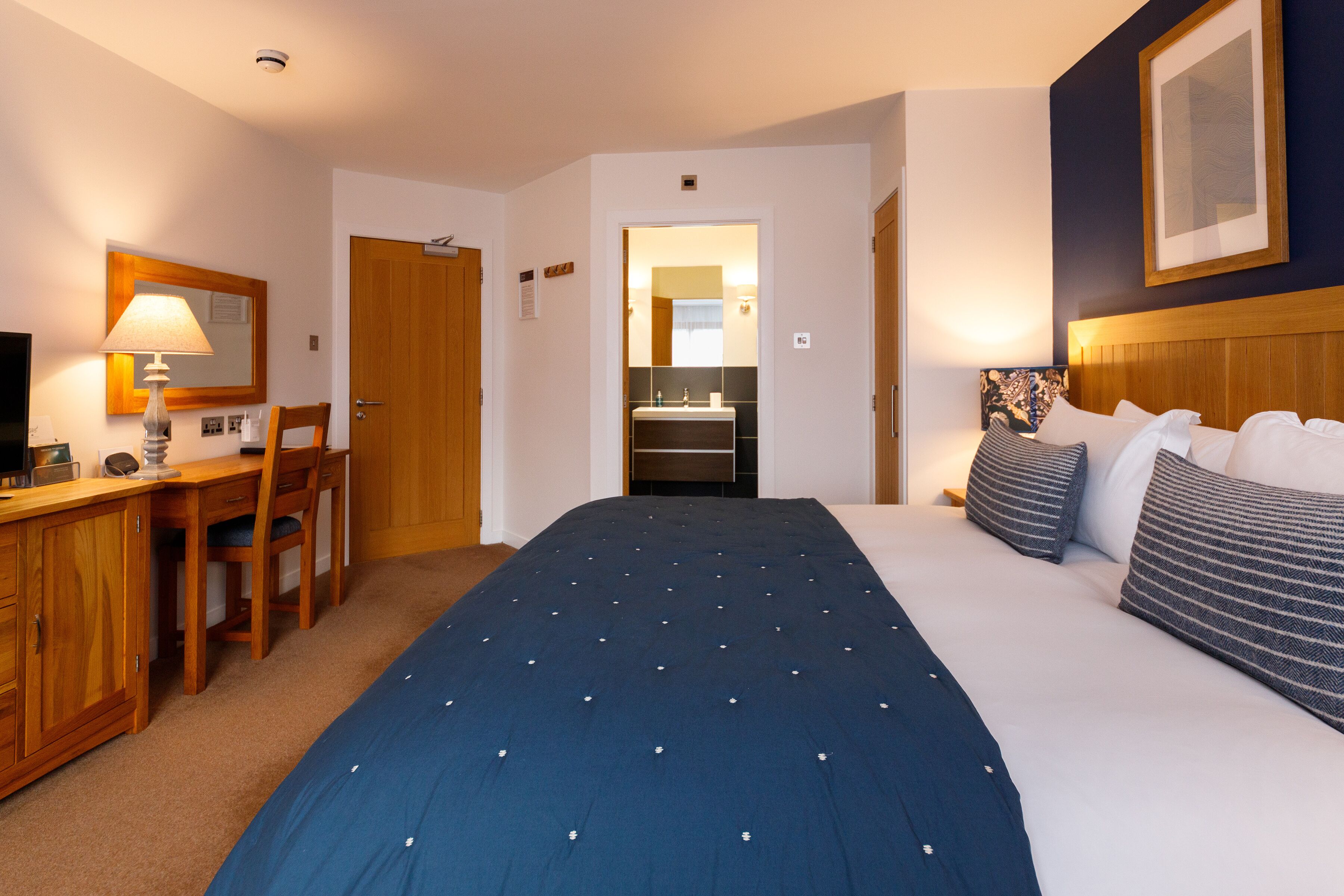 Une chambre d’hôtel avec un lit, un bureau et une chaise, une télévision et une salle de bain visible à travers une porte ouverte.