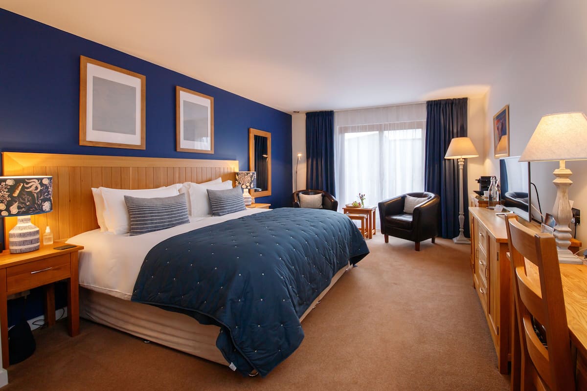 A hotel room with a large bed, a desk, a chair, and a nightstand.