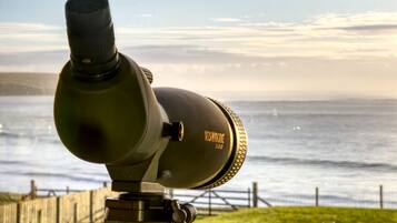A telescope with a view of the ocean and a wooden fence in the foreground.