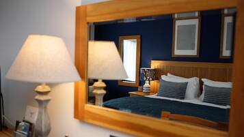 A hotel room with a large mirror reflecting the bed and nightstands, a lamp, and a framed picture on the wall.