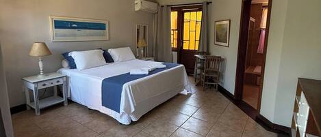 A hotel room with a large bed, a nightstand with a lamp, a chair, and a door leading to another room.